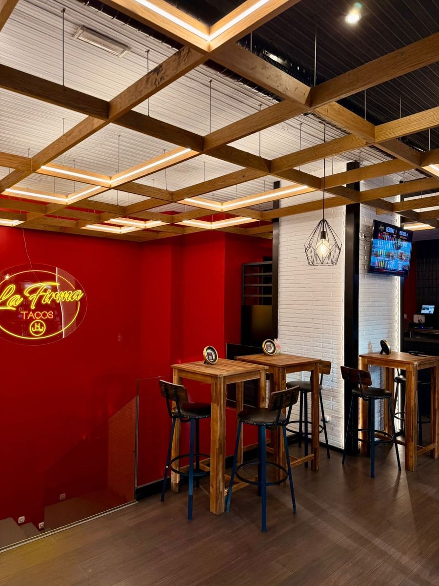 Letrero de neón La Firma Tacos sobre pared roja